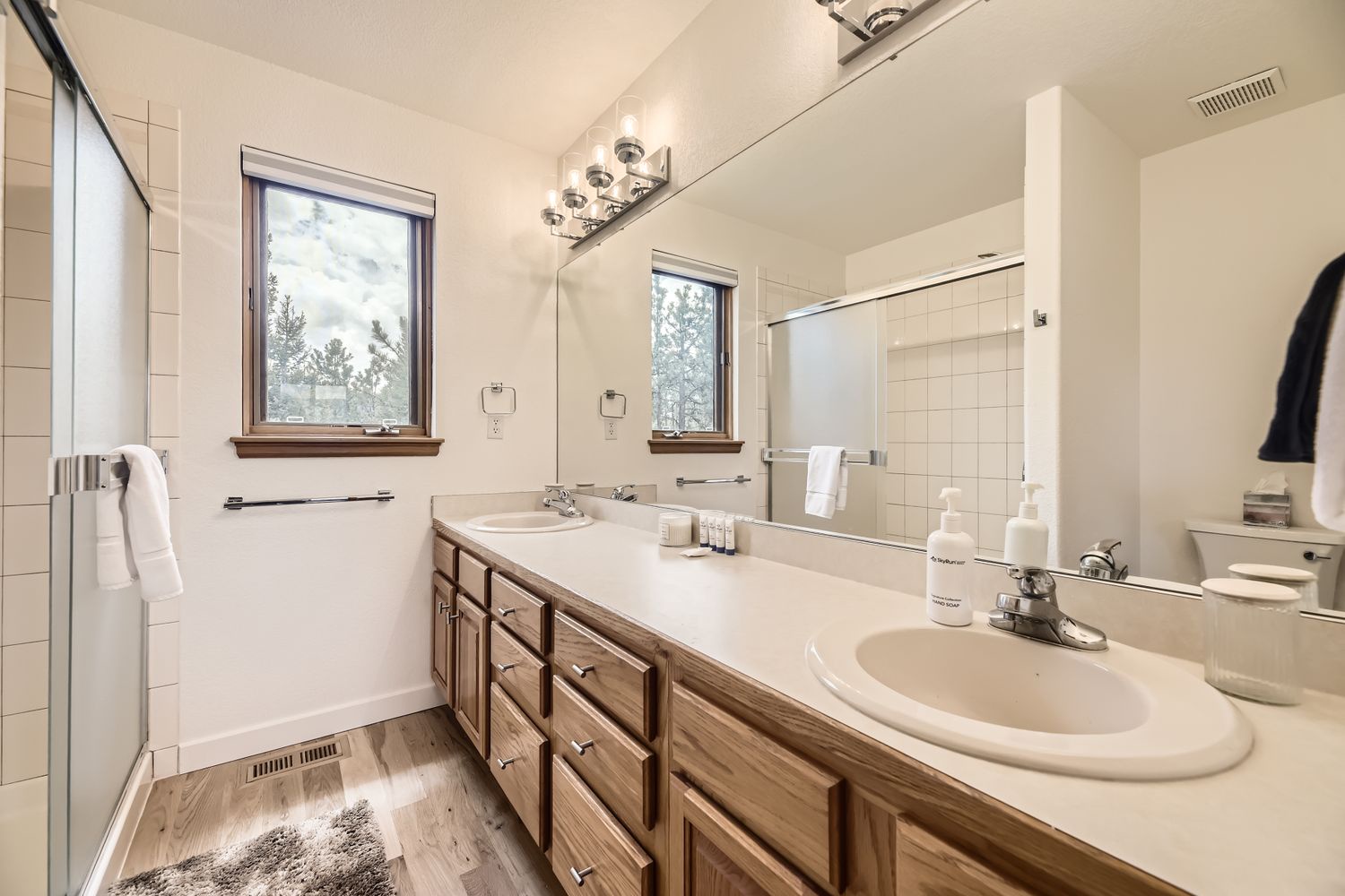Step into this spacious bathroom featuring dual sinks, elegant wood vanity, and natural light streaming through charming windows for your morning routine.