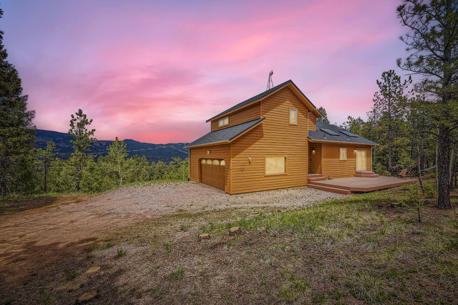 Modern cedar cabin nestled in forested mountains with stunning pink sunset skies and private gravel parking area.