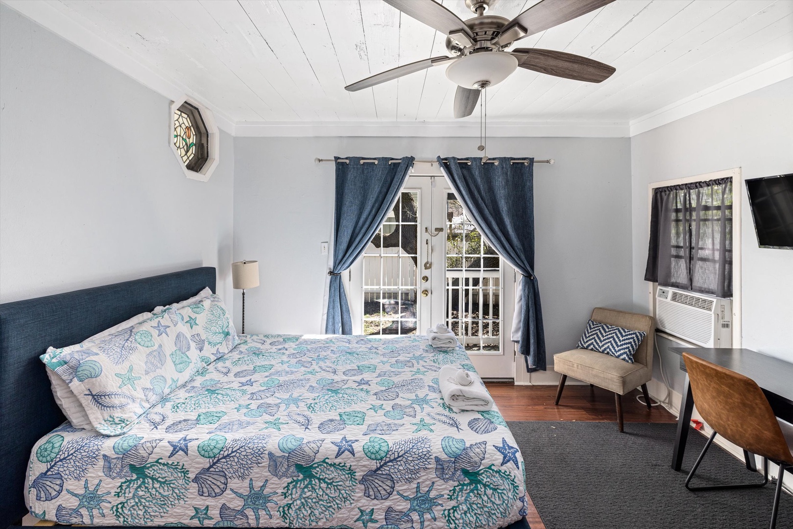 Relax in this coastal-themed bedroom featuring a comfortable bed with ocean-inspired linens, ceiling fan for gentle breezes, and French doors leading to your private balcony.