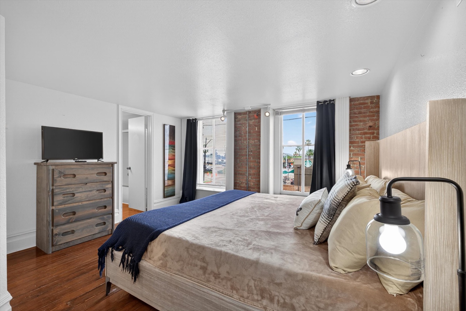 Bright bedroom with brick walls, hardwood floors, and views.