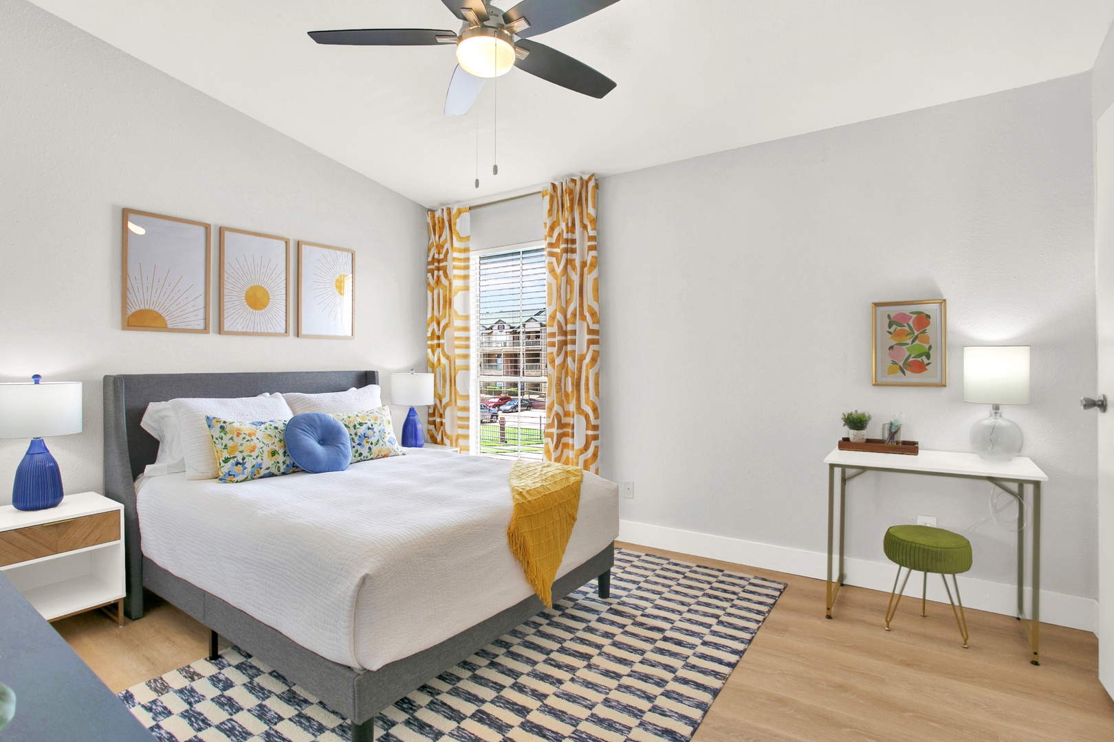 Bright bedroom with desk, fan, and plush bed.