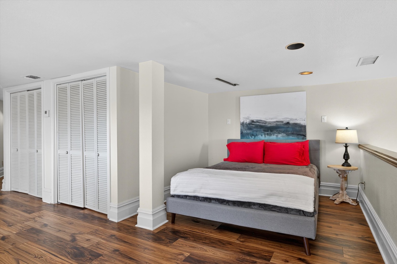 Bright bedroom with plush bed, red pillows, and closet.