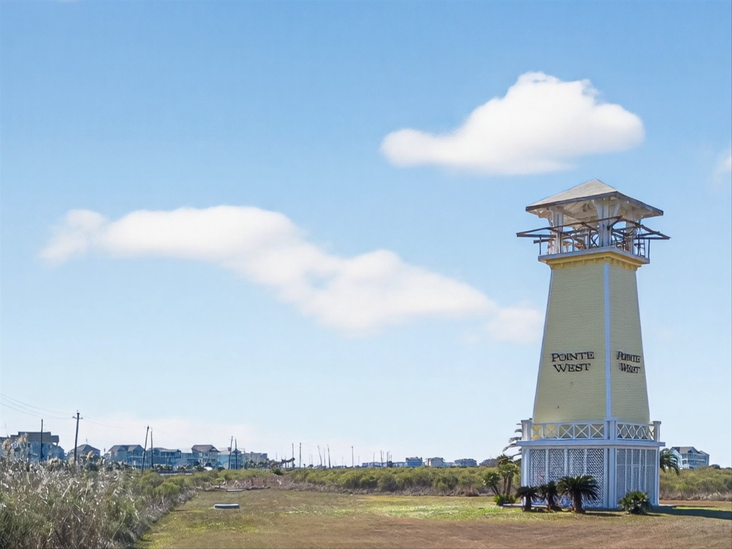 Coastal landmark lighthouse amid dunes and residences.