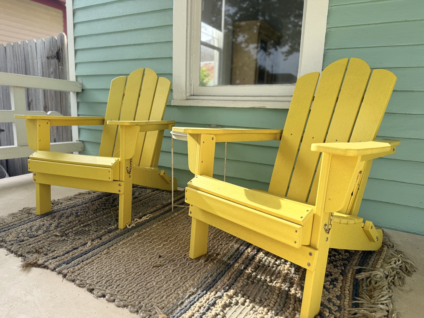 Settle into cheerful yellow Adirondack chairs on the front porch—perfect for morning coffee or evening relaxation against charming coastal cottage vibes.