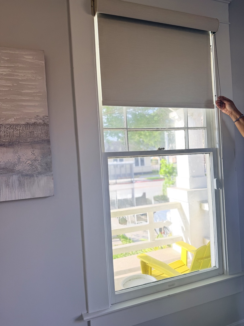 A bright window opens to a neighborhood view, where a cheerful yellow chair catches sunlight on the patio below. The shade is ready to adjust for your perfect amount of natural light.