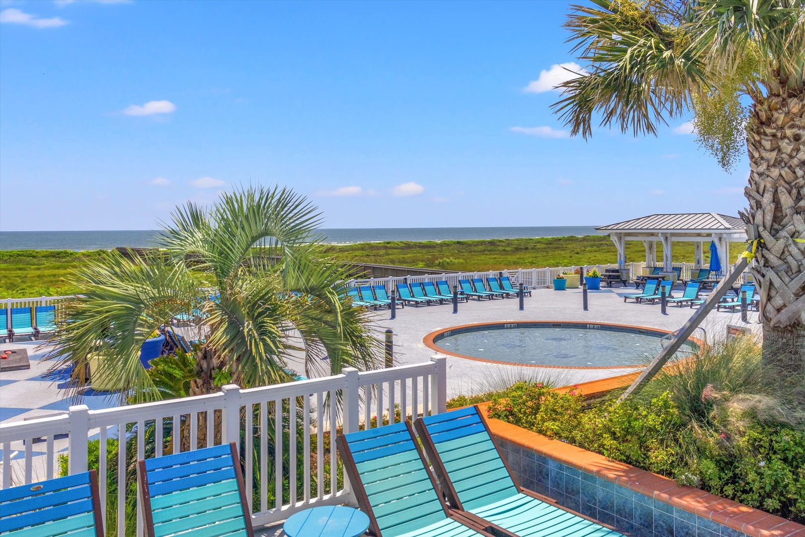 Tropical oceanfront pool deck with hot tub and palms.