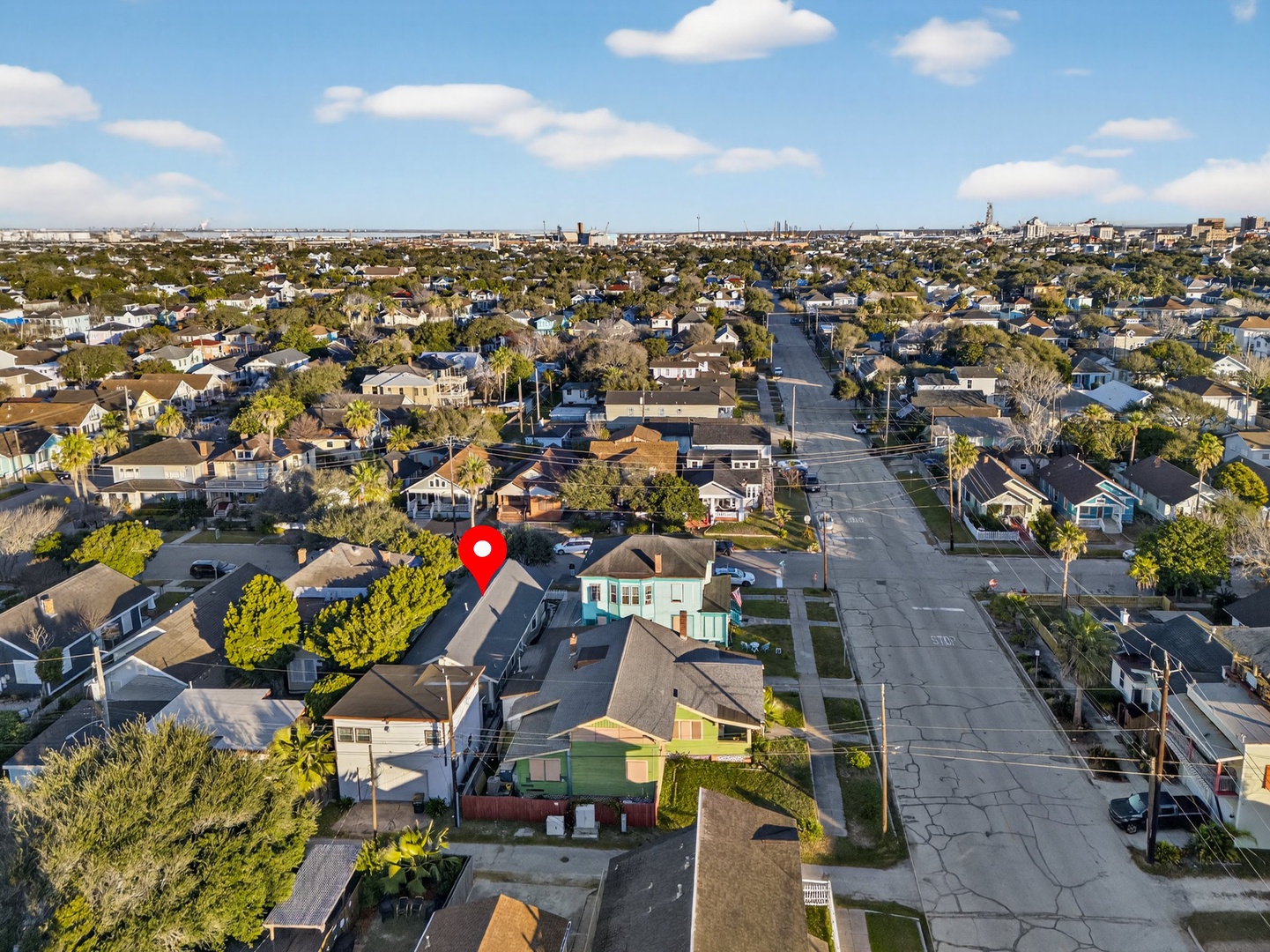Aerial view of a charming residential neighborhood with tree-lined streets and diverse housing styles under a bright blue sky.