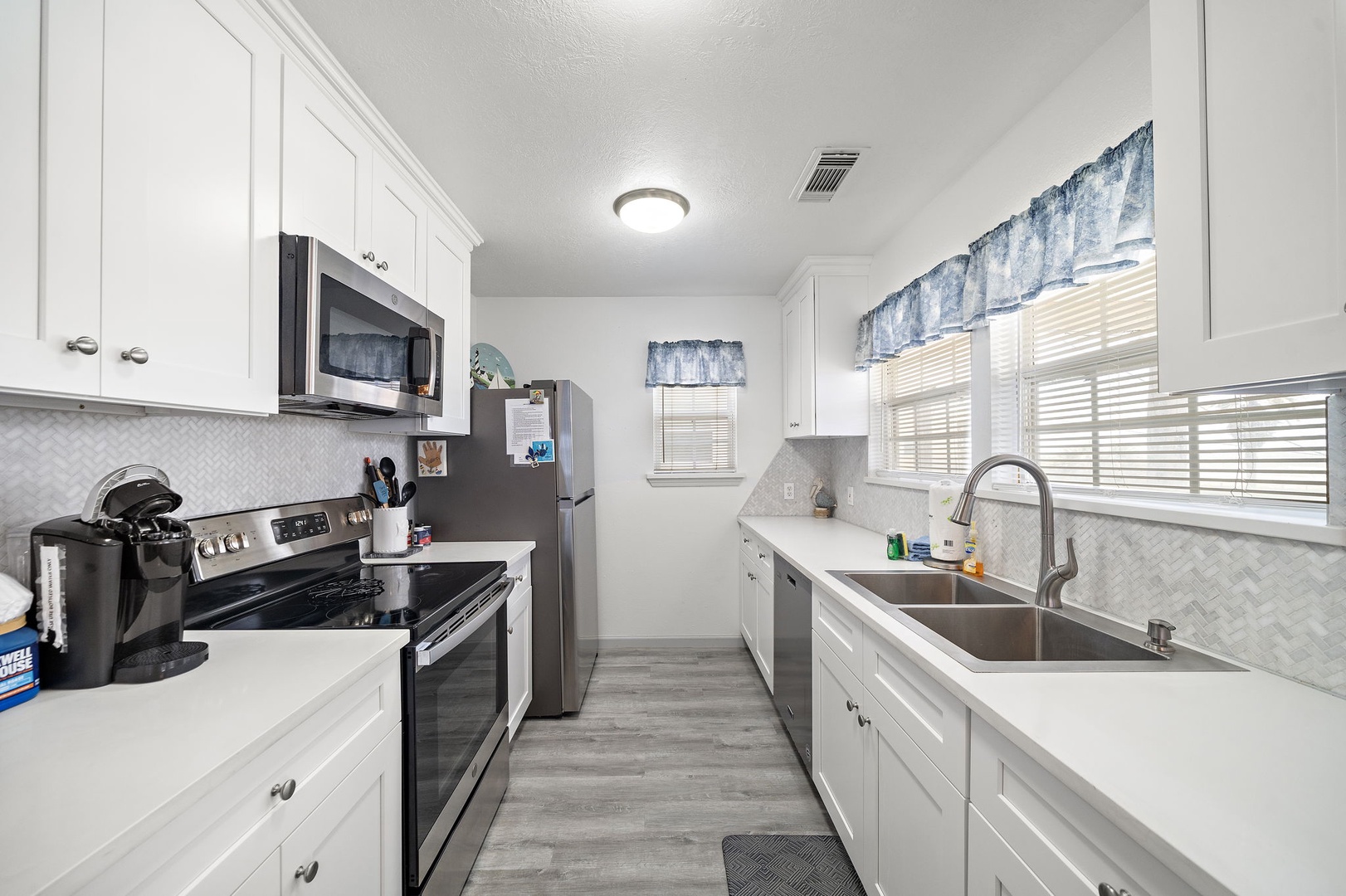 Step into your fully equipped galley kitchen where crisp white cabinets and modern appliances await your culinary adventures. Natural light filters through cheerful blue curtains as you prepare meals with everything you need at your fingertips.