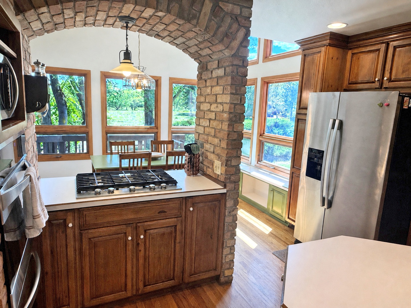 Your gourmet kitchen features a gas range island under a striking brick archway, warm wood cabinetry, and sunlit windows.
