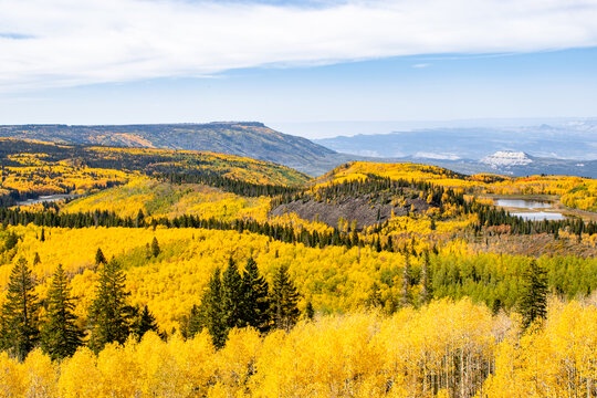 The surrounding area features stunning autumn foliage blanketing rolling hills and mountains, with golden aspens creating a breathtaking seasonal display against evergreen forests.