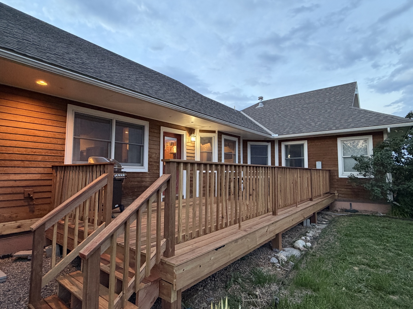 Welcoming property exterior with wooden deck and warm evening lighting under cloudy skies.