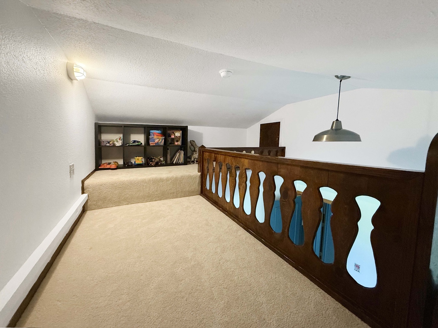 This loft space offers a cozy retreat with plush carpeting, vintage wooden railings, and handy built-in shelving for your books and treasures.