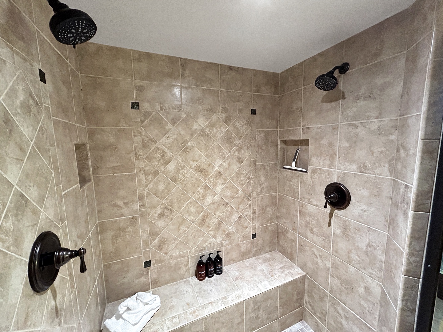 Luxurious dual-head shower with elegant travertine tiles and built-in bench - your perfect retreat for relaxing after exploring.