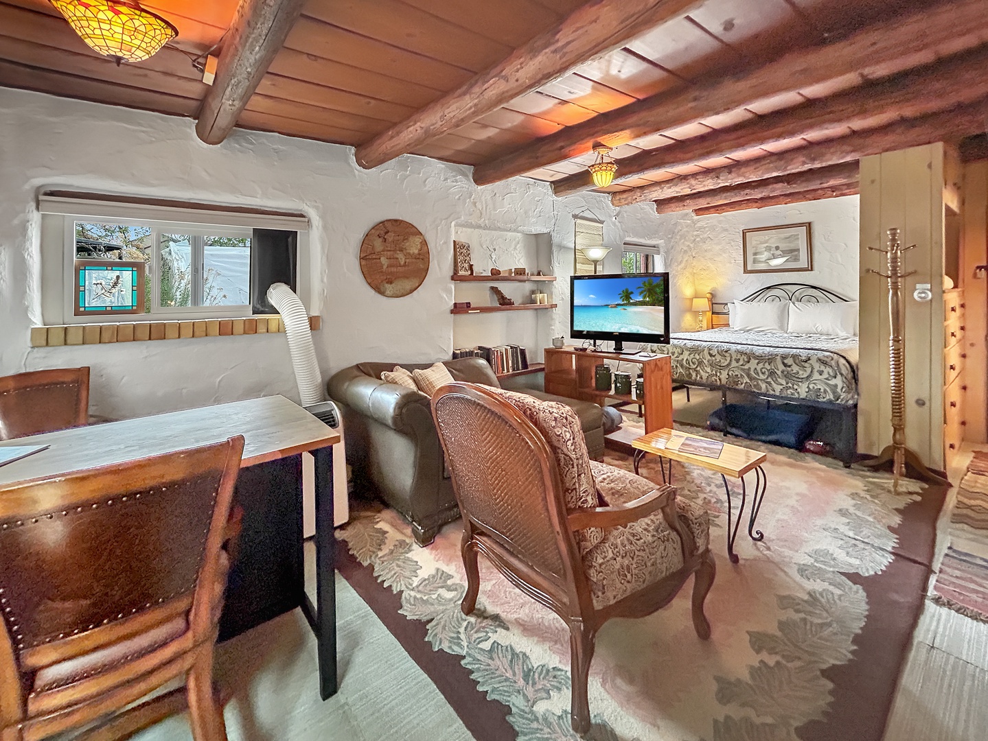 Relax in your charming studio where rustic beams frame cozy seating, a comfortable bed, and modern amenities blend seamlessly.