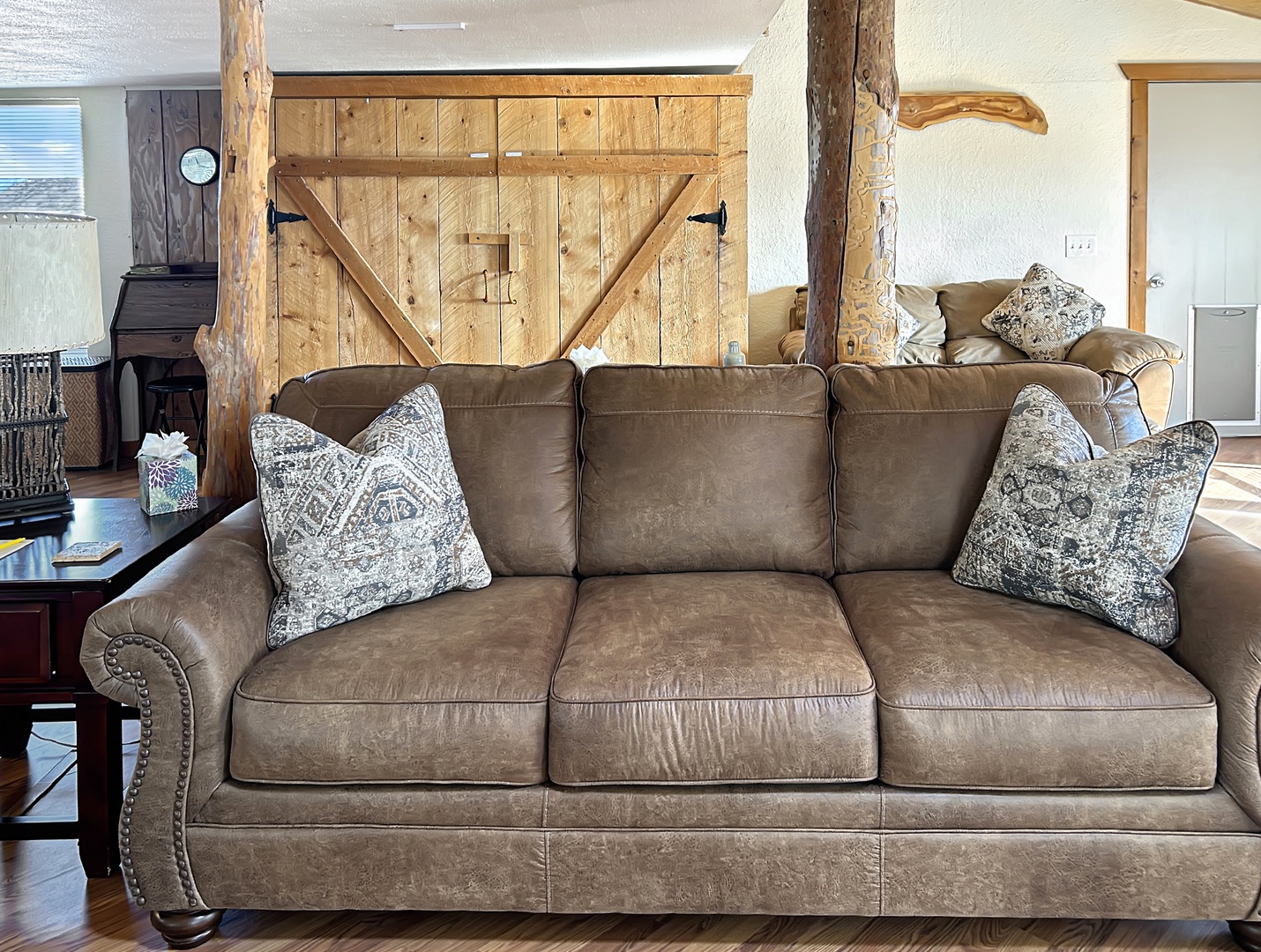 Sink into this plush leather sofa surrounded by rustic wood beams and barn doors, creating your perfect mountain retreat atmosphere.