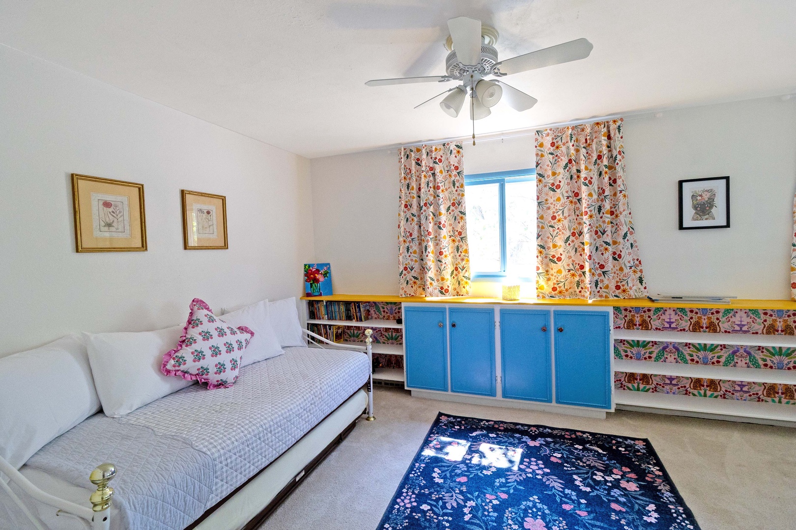 Relax on your daybed in this cheerful room, where floral curtains frame the window and colorful storage keeps your belongings tidy and within reach.