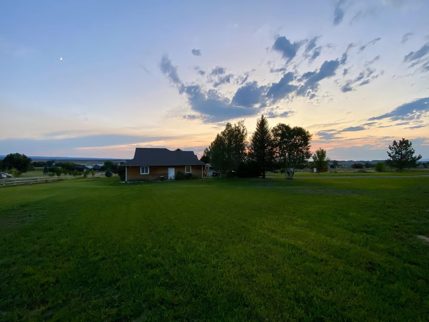 Peaceful countryside property with stunning sunset backdrop, framed by tall trees.