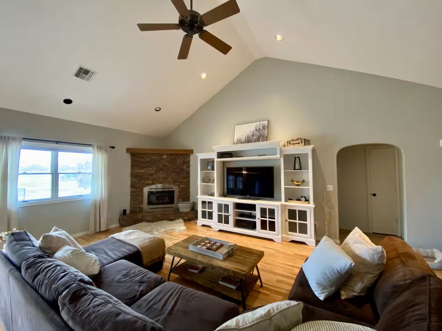 Spacious living room with vaulted ceilings, cozy seating, natural light and a warm fireplace.