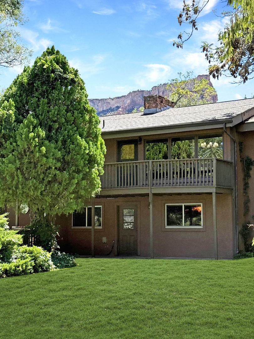 Set against dramatic desert cliffs, this property features a deck overlooking manicured lawns and mature trees, creating a peaceful retreat in a stunning natural setting.