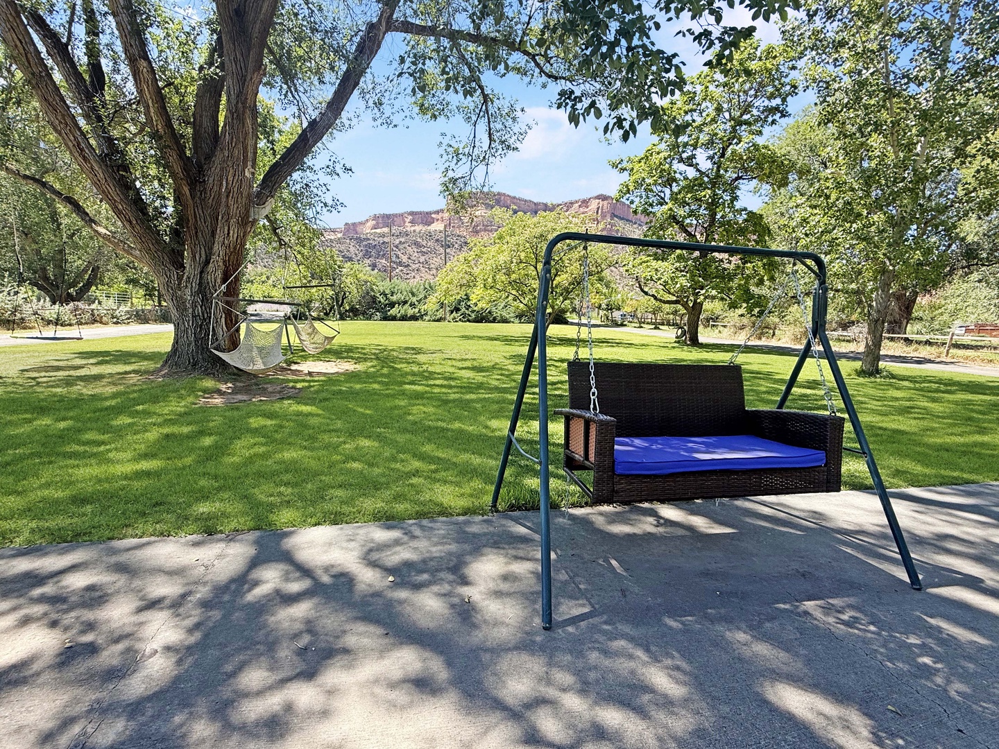 A property nestled amid mature trees and lush green lawns, with striking red rock formations visible in the surrounding landscape.