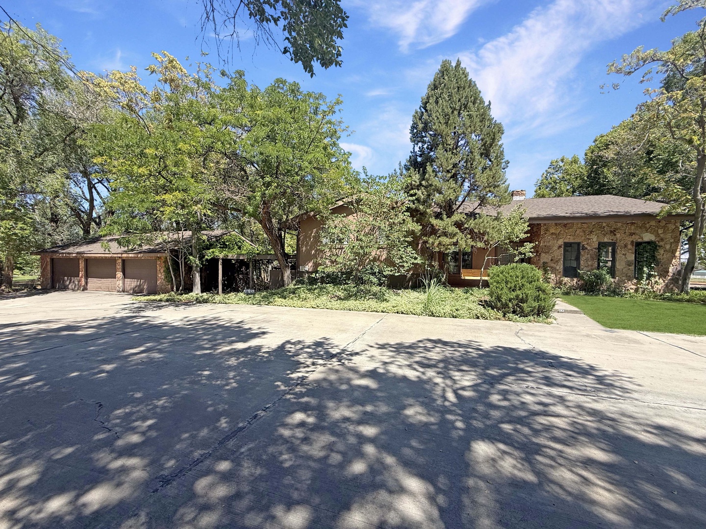 A charming brick and stucco property surrounded by mature trees and lush landscaping, with ample parking and a peaceful, tree-lined setting.