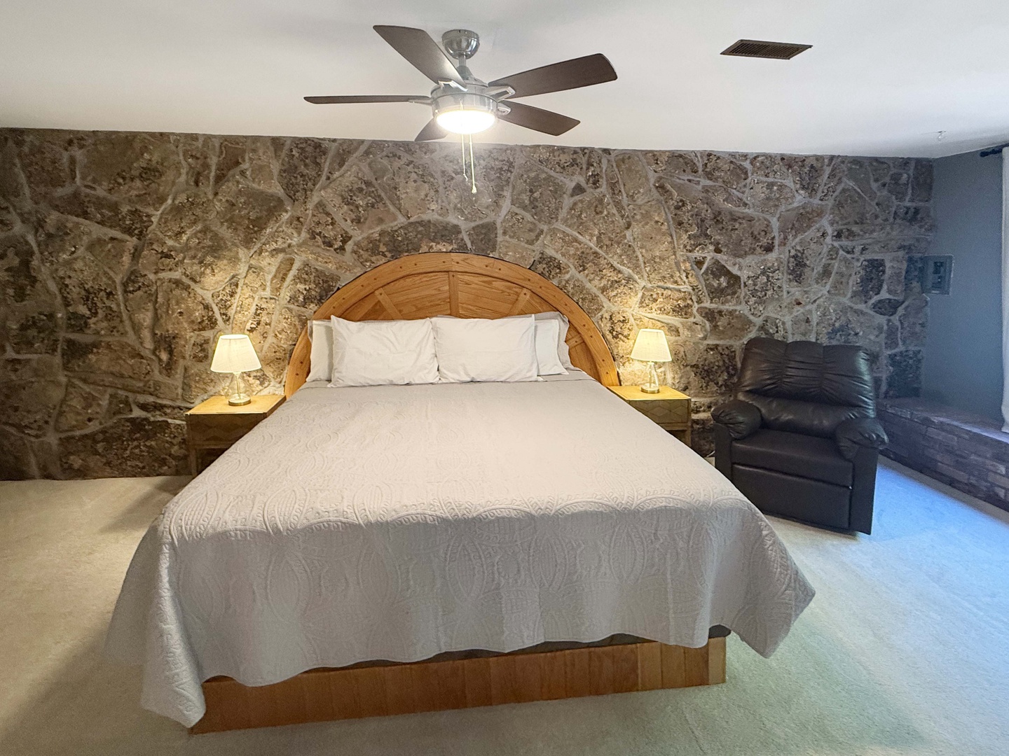Unwind in your serene bedroom, where textured stone walls meet warm lighting and plush bedding, creating a cozy escape perfect for restful nights.