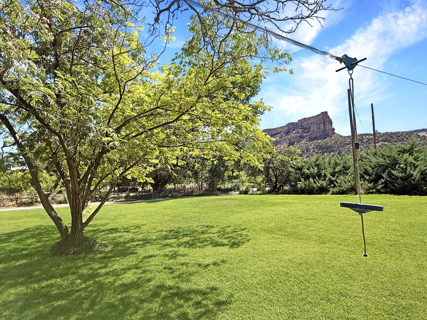A spacious lawn with shaded trees and a zip line set against the stunning backdrop of red rock formations.