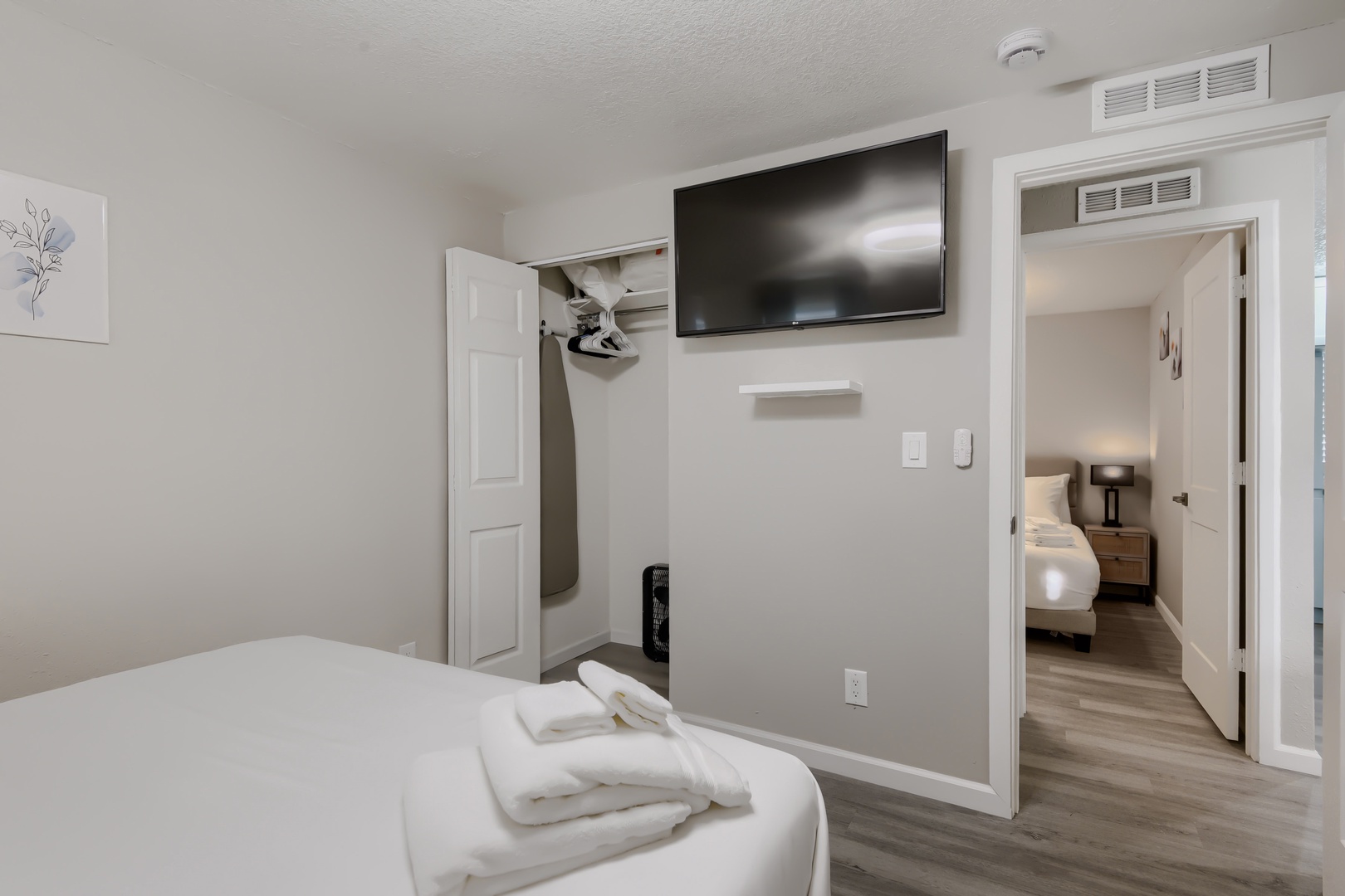 Primary bedroom with wall-mounted TV and closet with iron and board