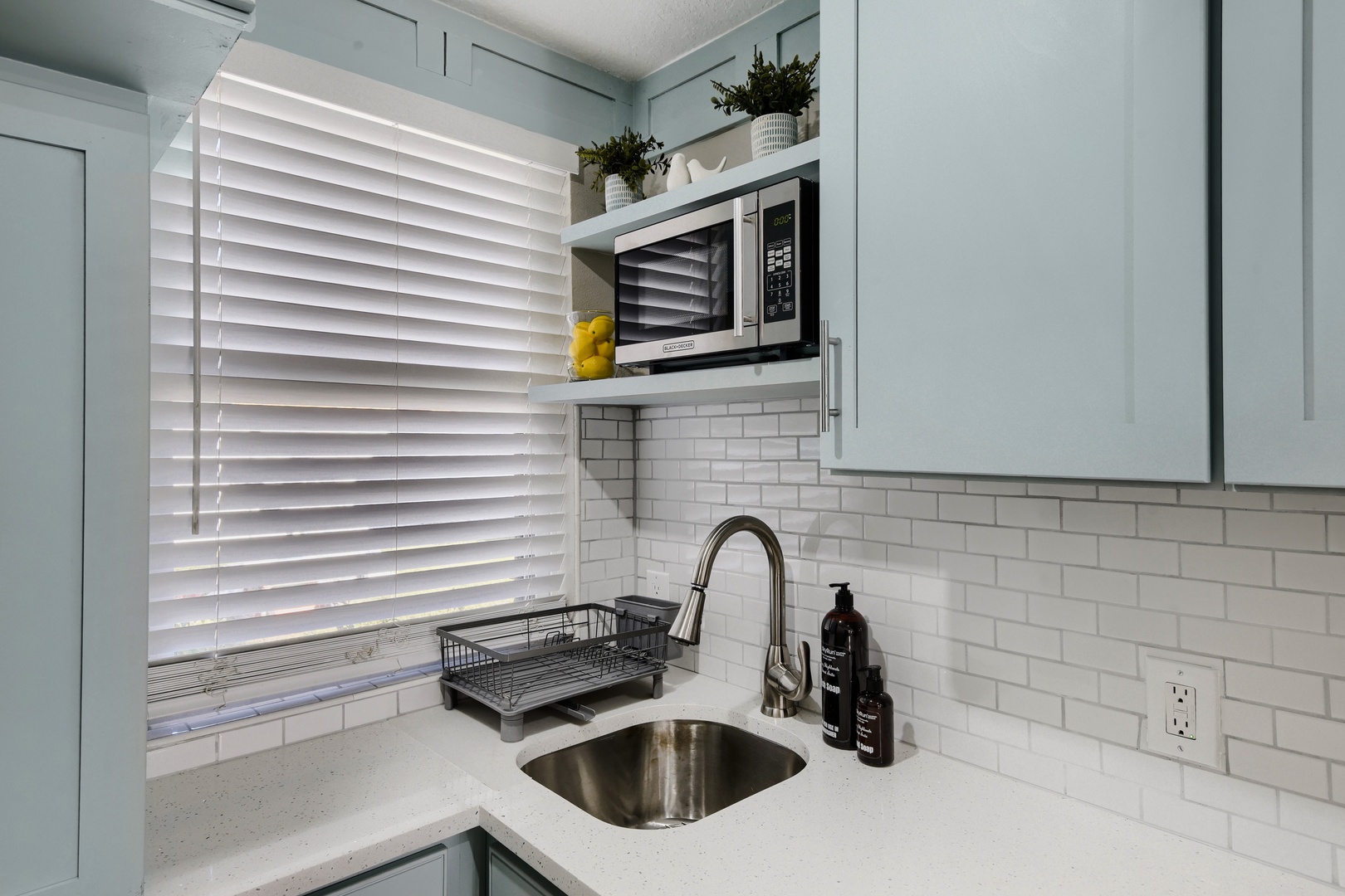 Kitchen sink, microwave, and subway tile backsplash