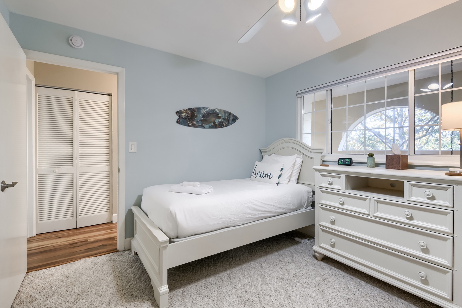 Twin bed beside a roomy dresser and sunny window