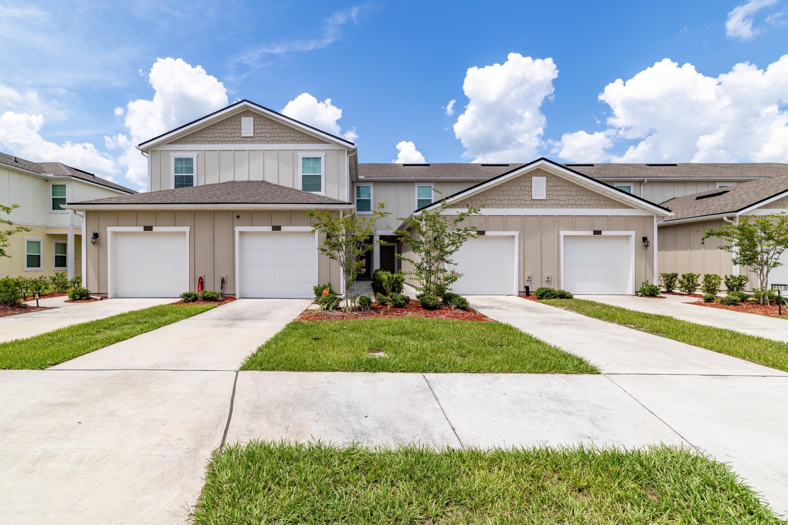 Modern residential property featuring attached townhome units with private garages, surrounded by manicured landscaping and fresh greenery throughout the community.