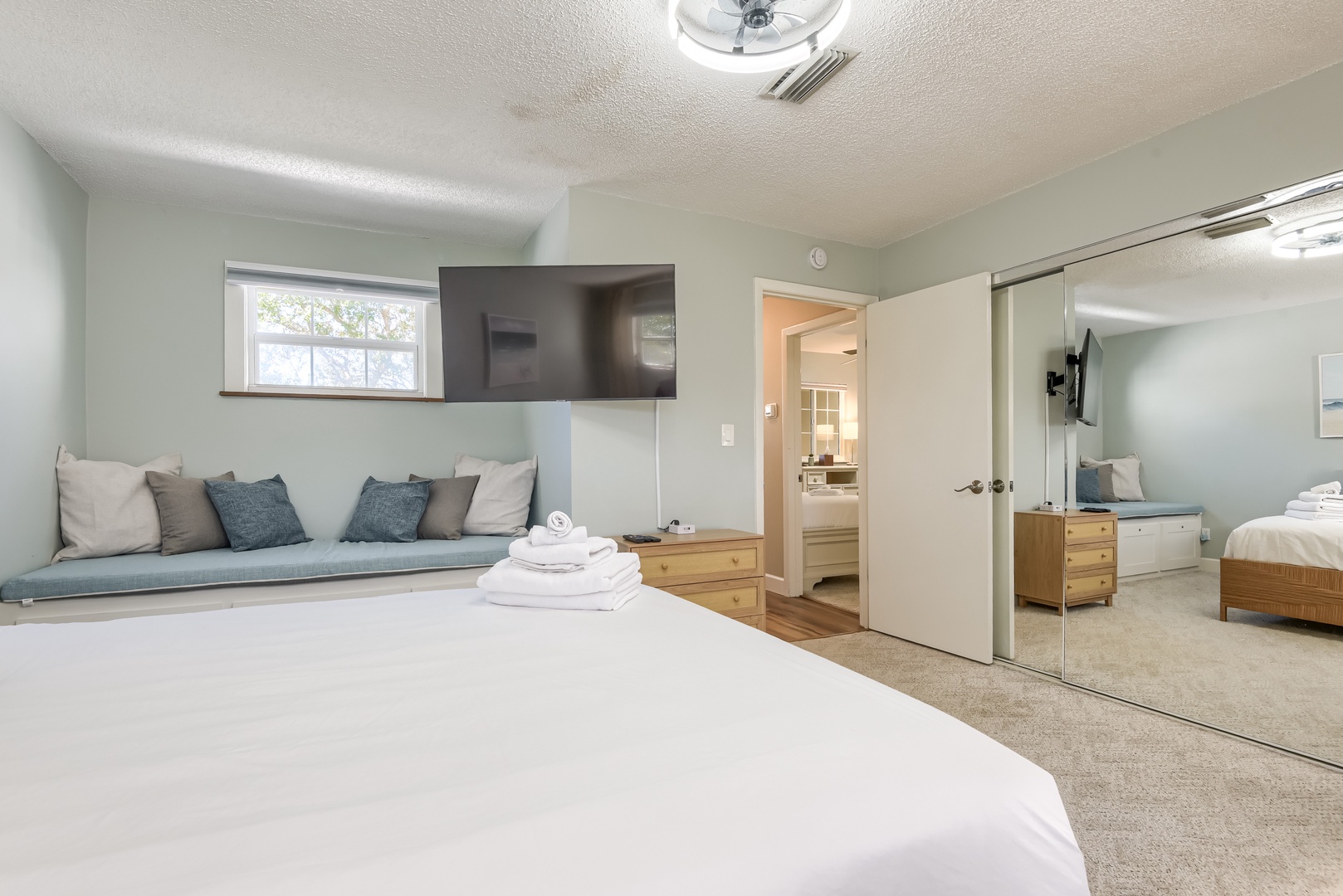 Primary bedroom with mirrored closet doors, TV and fresh towels