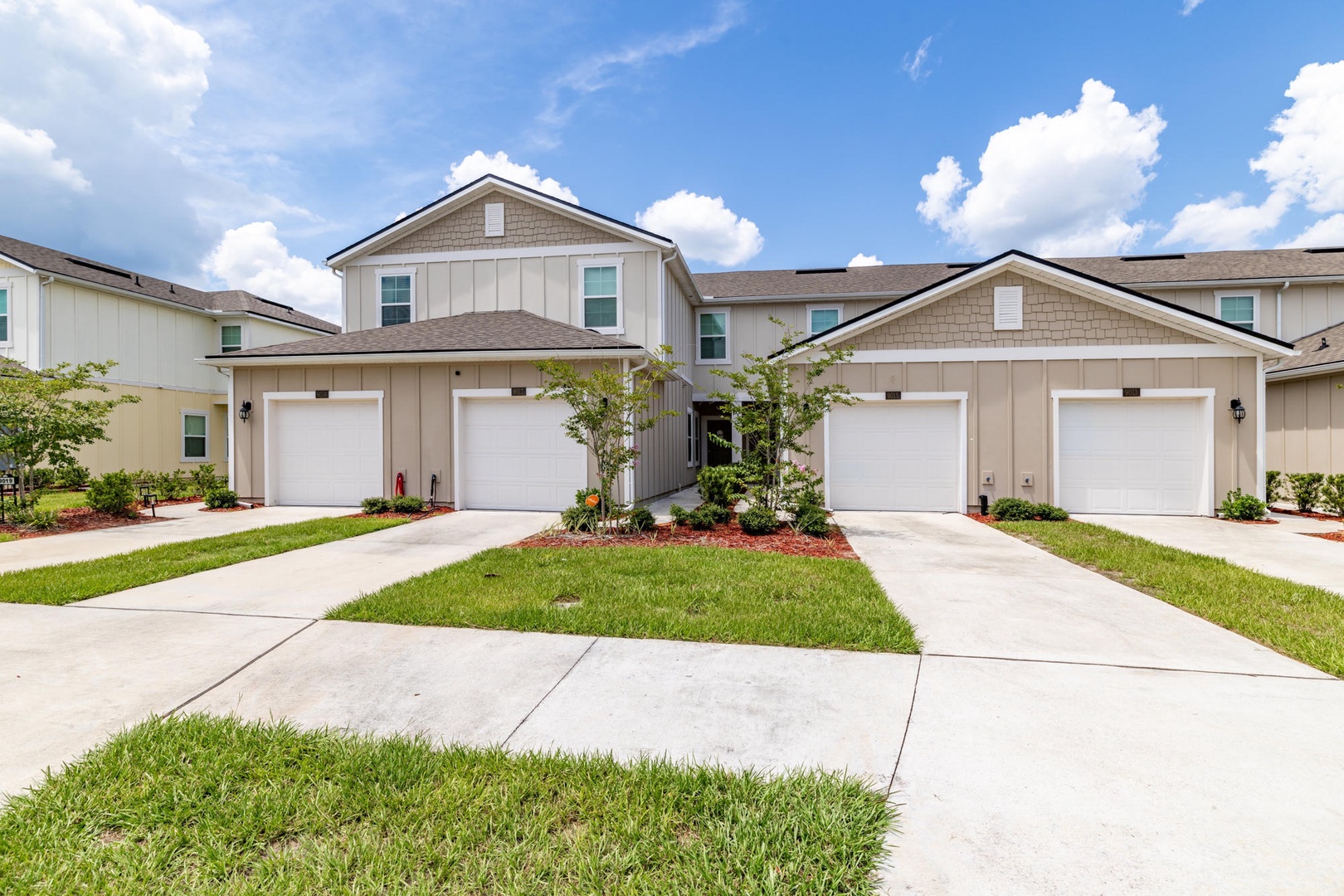 This modern townhome-style building features private garages and well-maintained landscaping, set within a quiet neighborhood under sunny skies.