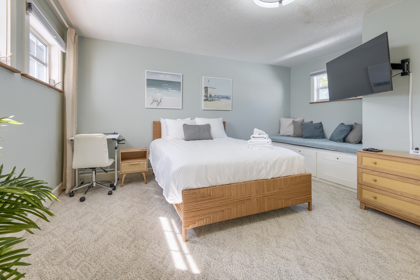 Spacious primary bedroom with a plush bed, window seat, desk and TV