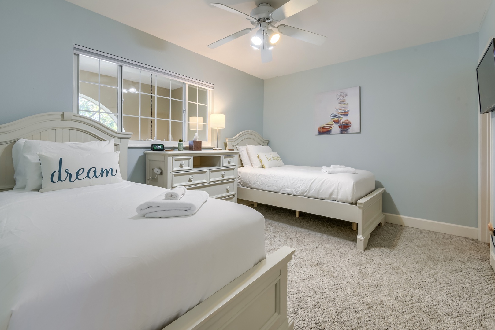 Bright twin bedroom with ceiling fan, TV and soft carpet