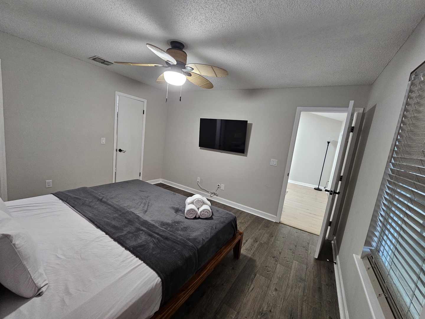 Your modern bedroom features fresh linens, a wall-mounted TV, and ceiling fan for your comfort, with fluffy towels waiting.