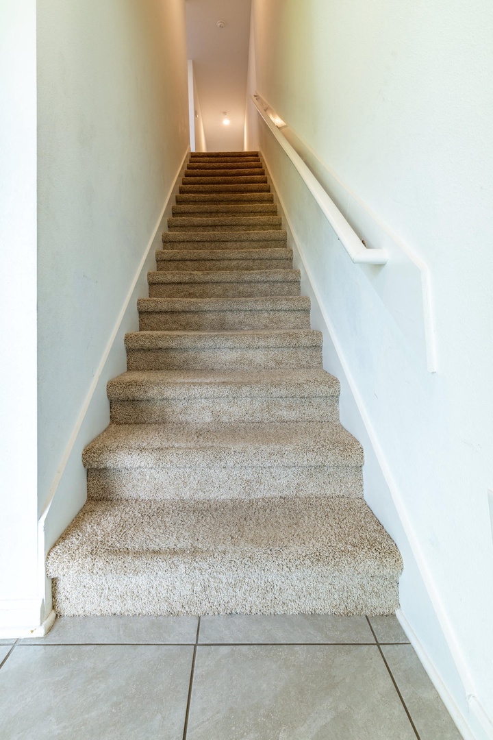 Carpeted staircase with handrails leads you to the upper level, softly lit to guide your way up safely and comfortably.
