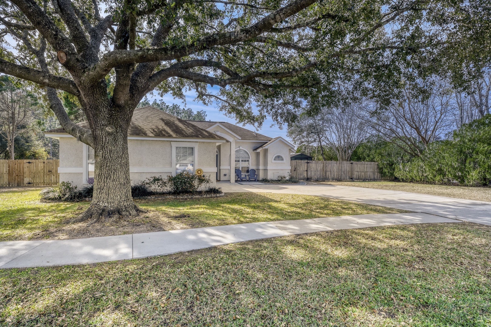 A beautiful single-story home nestled under mature oak trees in a peaceful residential neighborhood with spacious driveway parking.