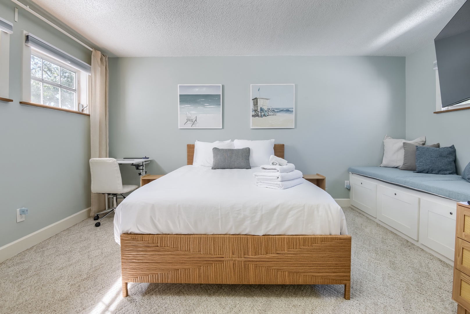 Serene primary bedroom with soft blue walls, storage bench and workspace