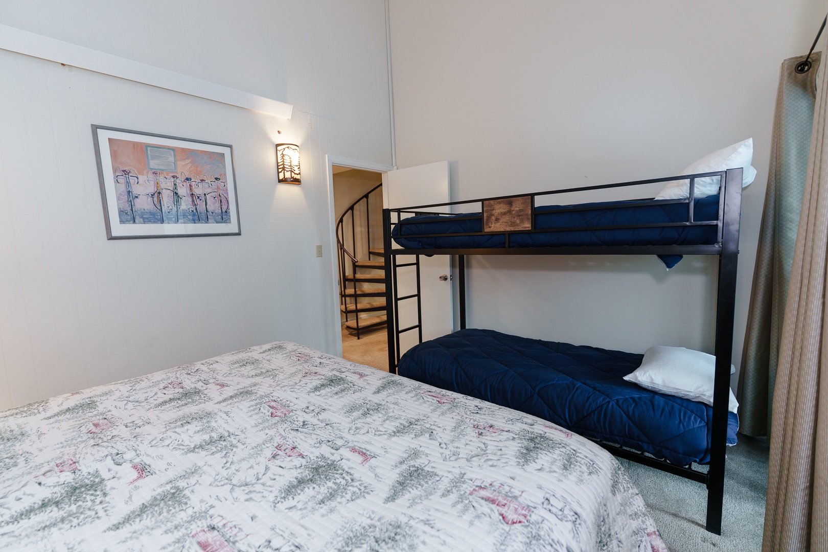 Your family bedroom features a comfortable queen bed alongside modern bunk beds, perfect for accommodating kids or extra guests in this cozy space with charming spiral stair access.