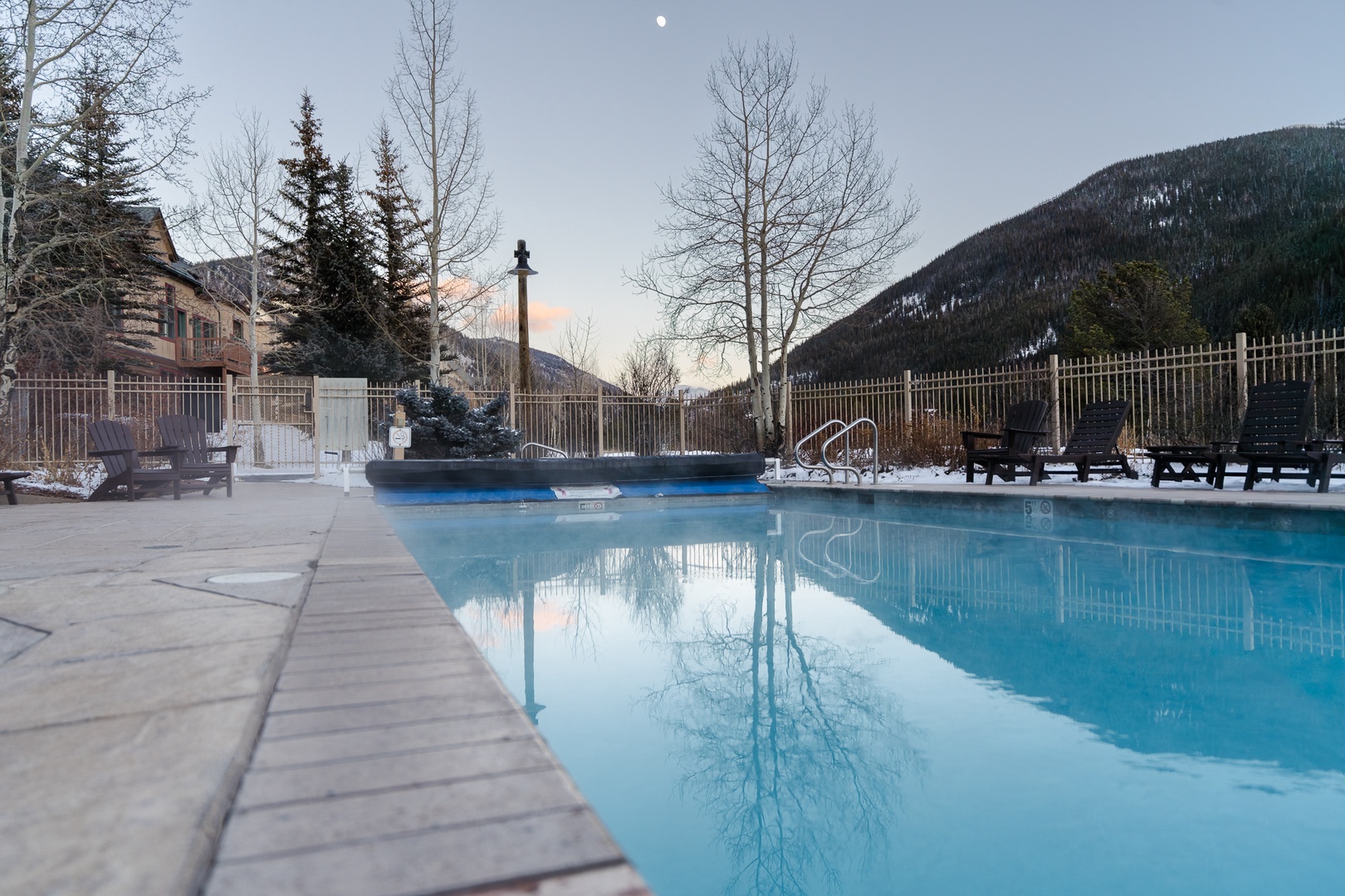 The property features a heated outdoor swimming pool surrounded by dramatic mountain scenery and winter forest landscape.