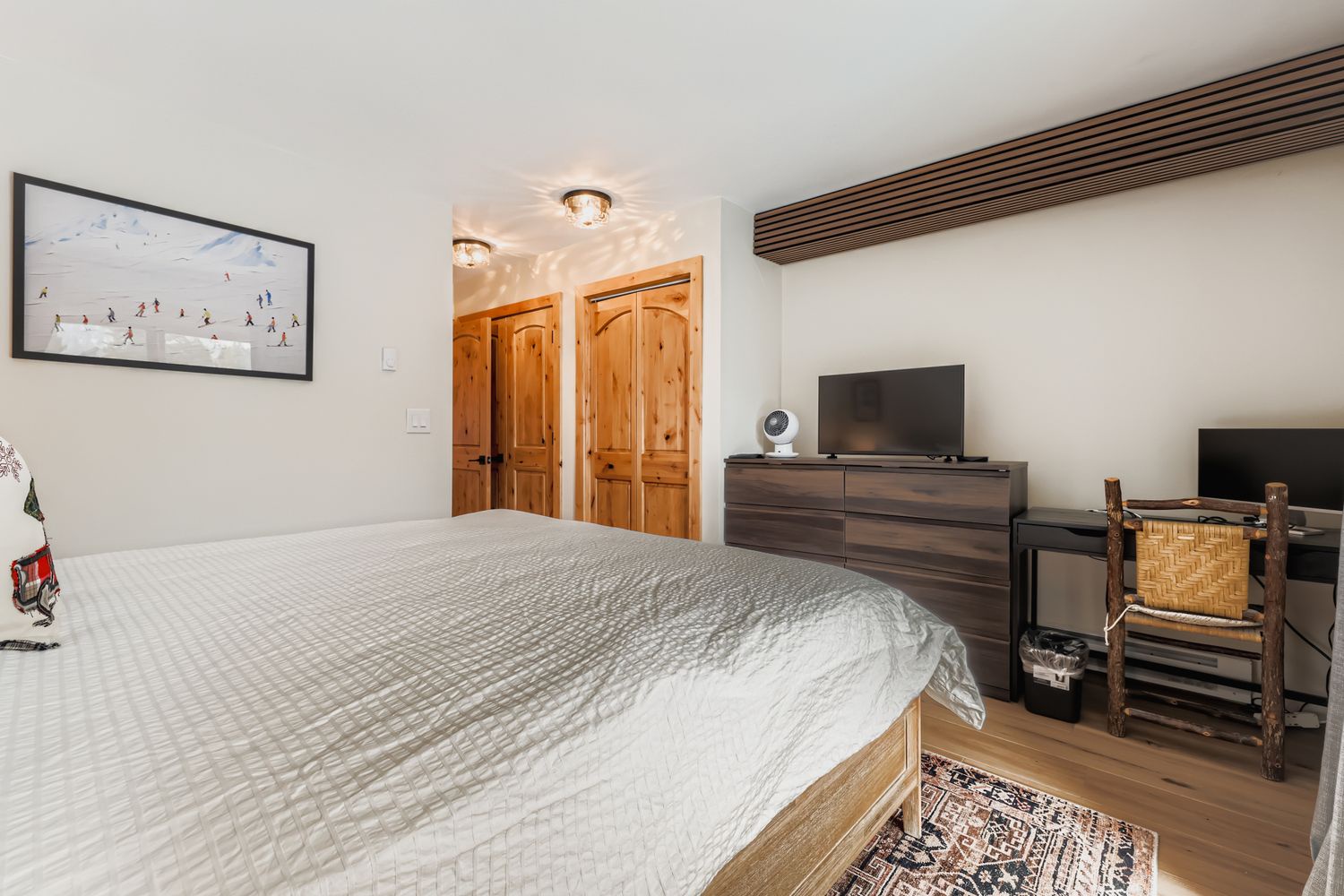 Sink into comfort in your cozy bedroom featuring a plush queen bed, modern entertainment center, and ski-themed artwork creating the perfect mountain retreat ambiance.