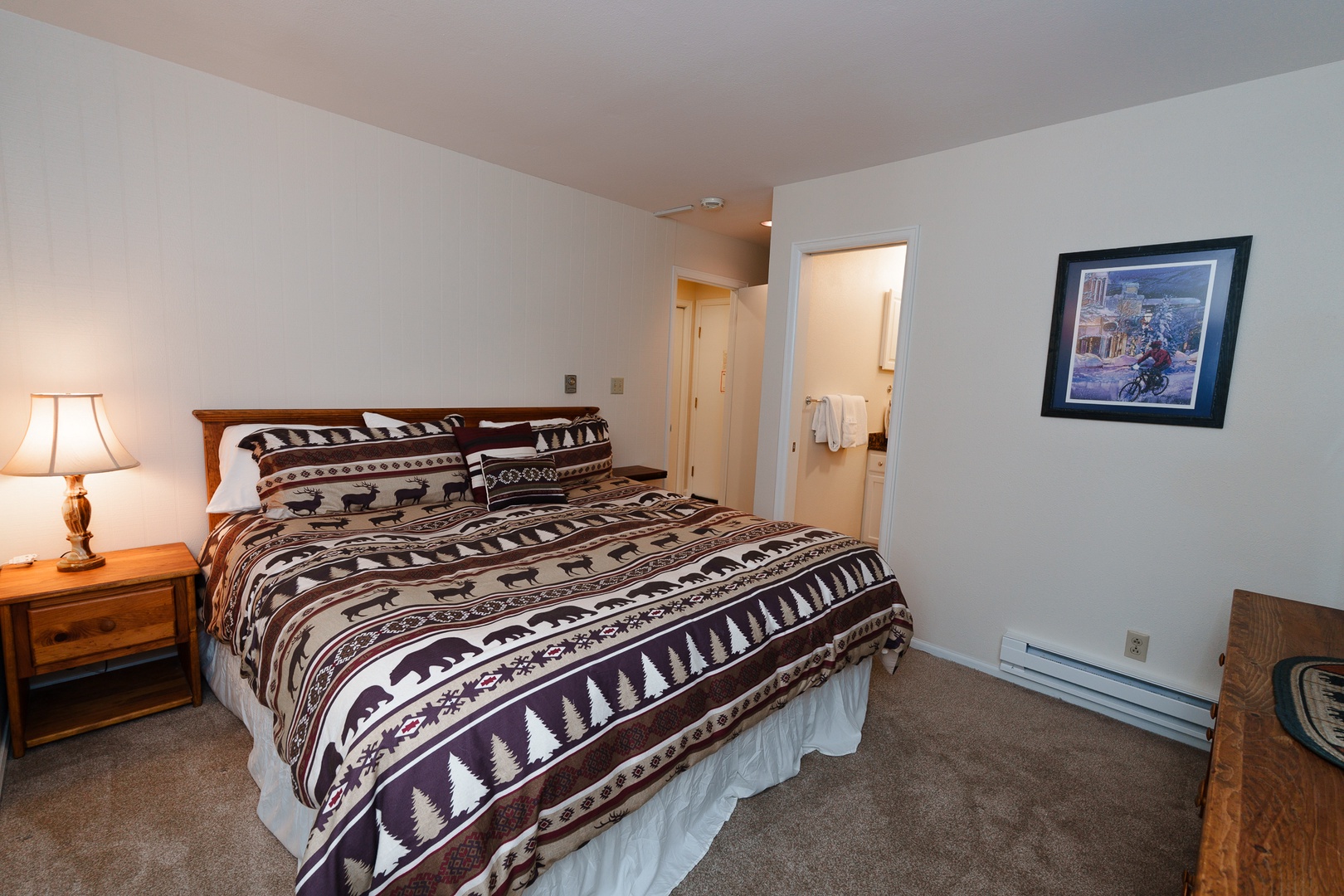 Relax in the cozy primary bedroom featuring rustic mountain-themed decor, comfortable furnishings, and a convenient en-suite bathroom for your mountain getaway.
