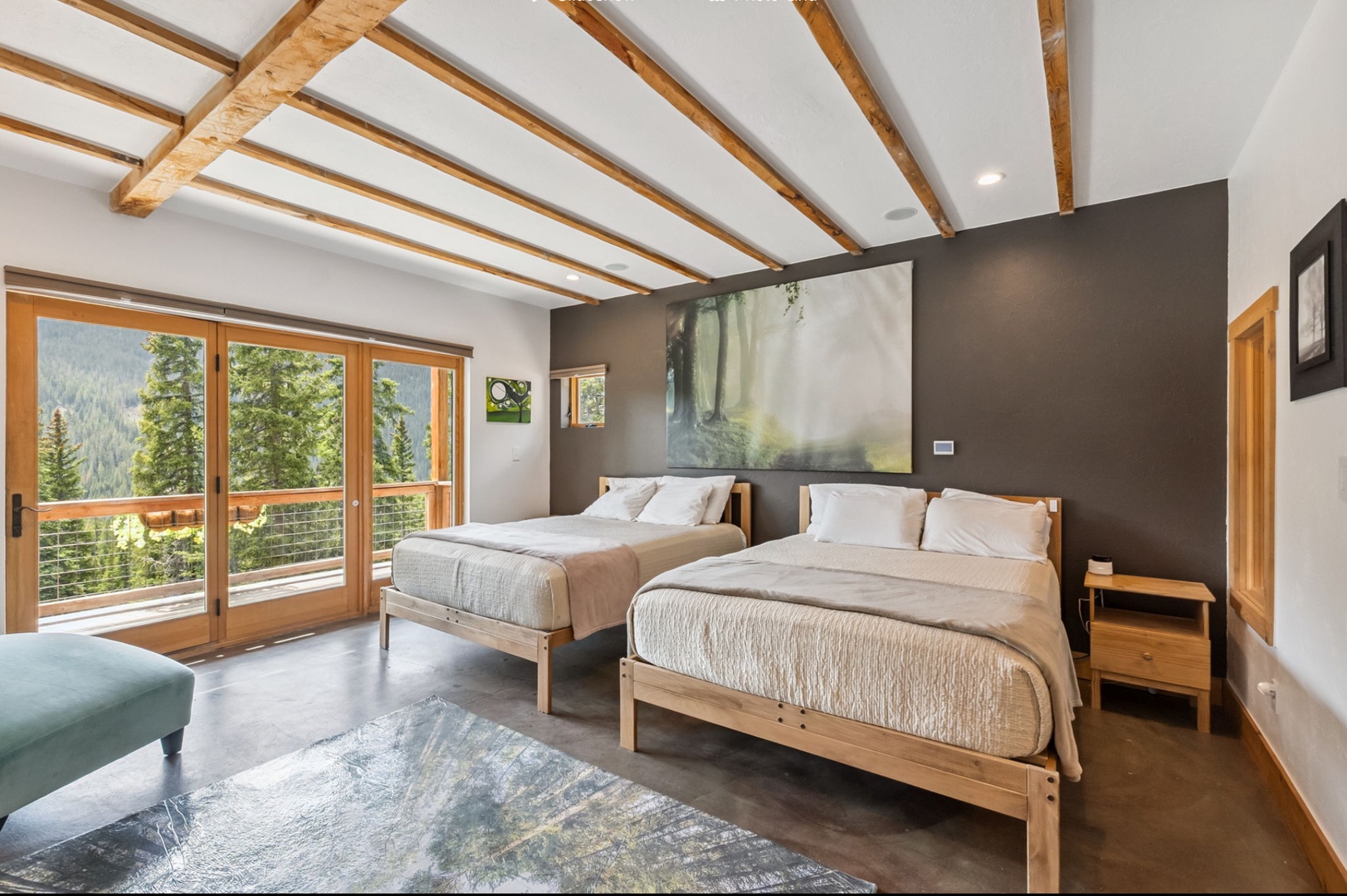 Rest in this spacious bedroom with two plush beds, soaring timber-beamed ceilings, and stunning forest views through floor-to-ceiling glass doors that open to your private deck.