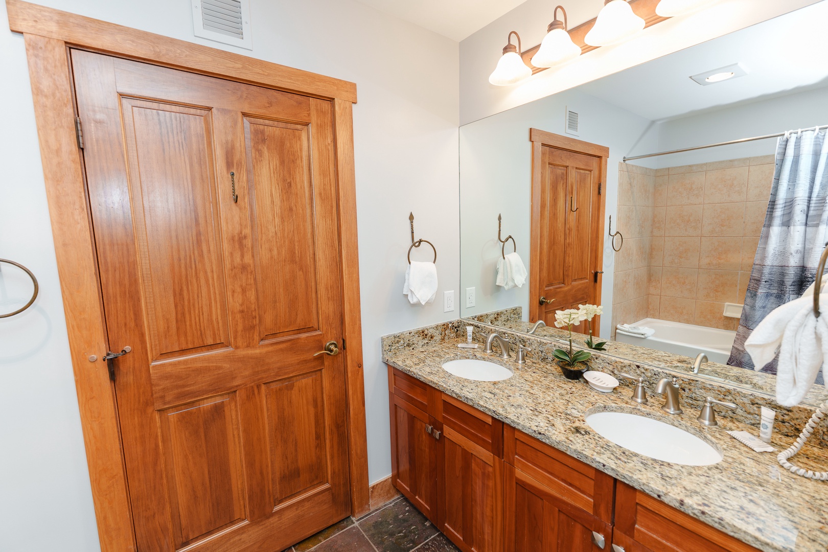 Refresh and prepare for your day in this elegant bathroom featuring dual vanities with granite countertops, warm wood cabinetry, and ample storage space for your stay.