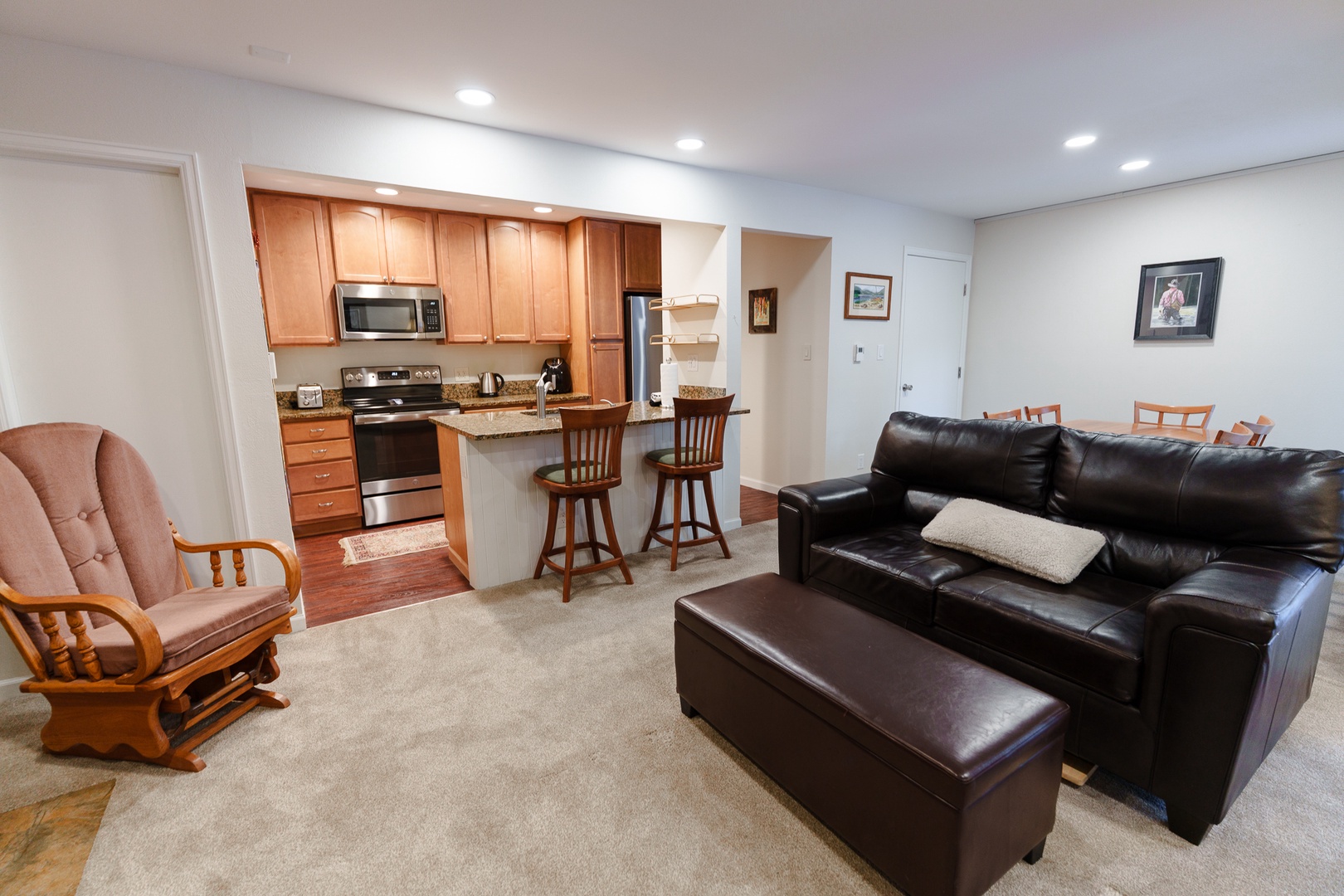Relax in your spacious living area with comfortable leather seating and enjoy easy access to the fully equipped kitchen featuring warm wood cabinets and modern appliances.