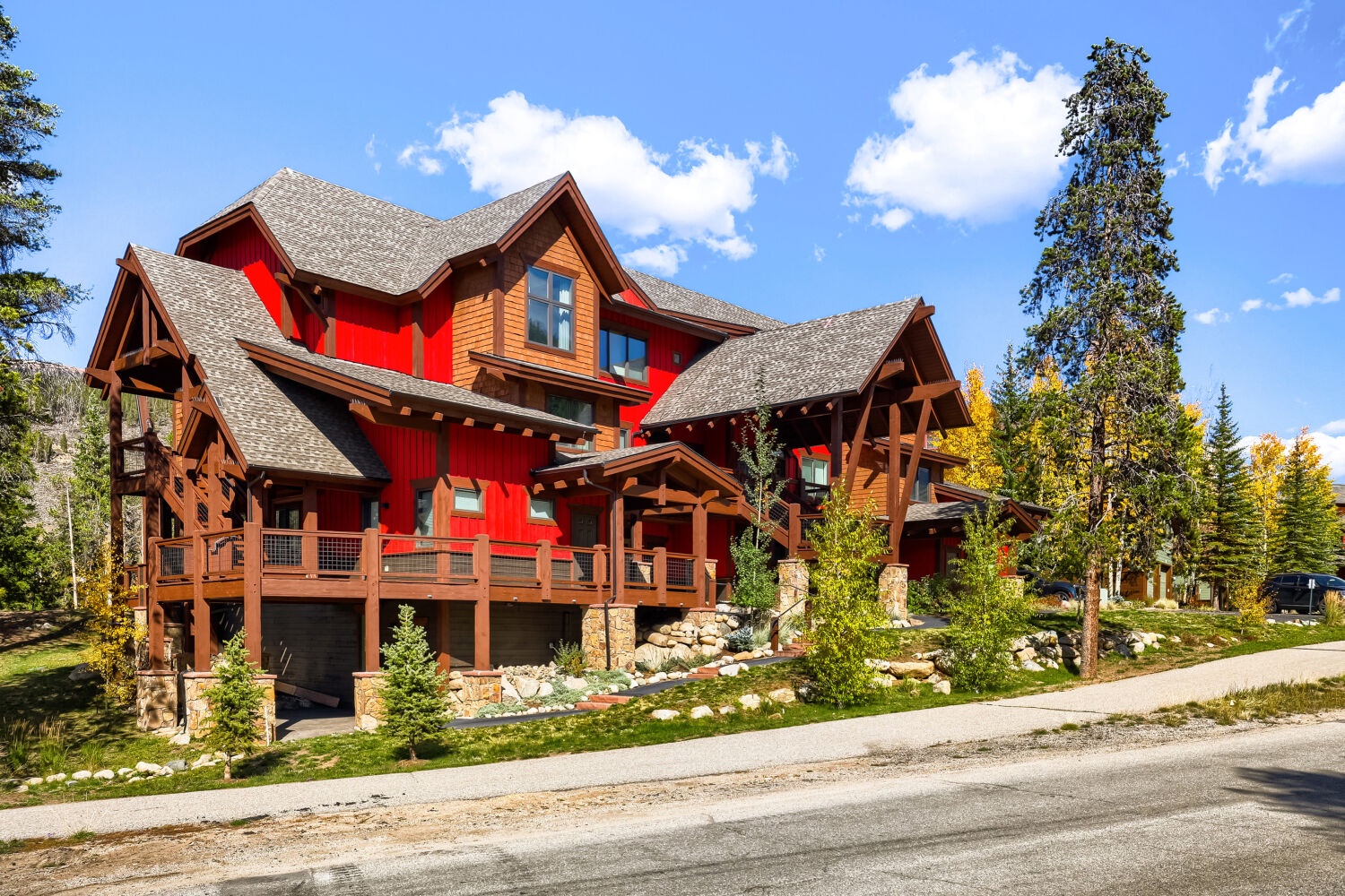 A distinctive mountain lodge featuring striking red and timber architecture, nestled among evergreens with seasonal foliage creating a vibrant autumn backdrop in a peaceful mountain setting.