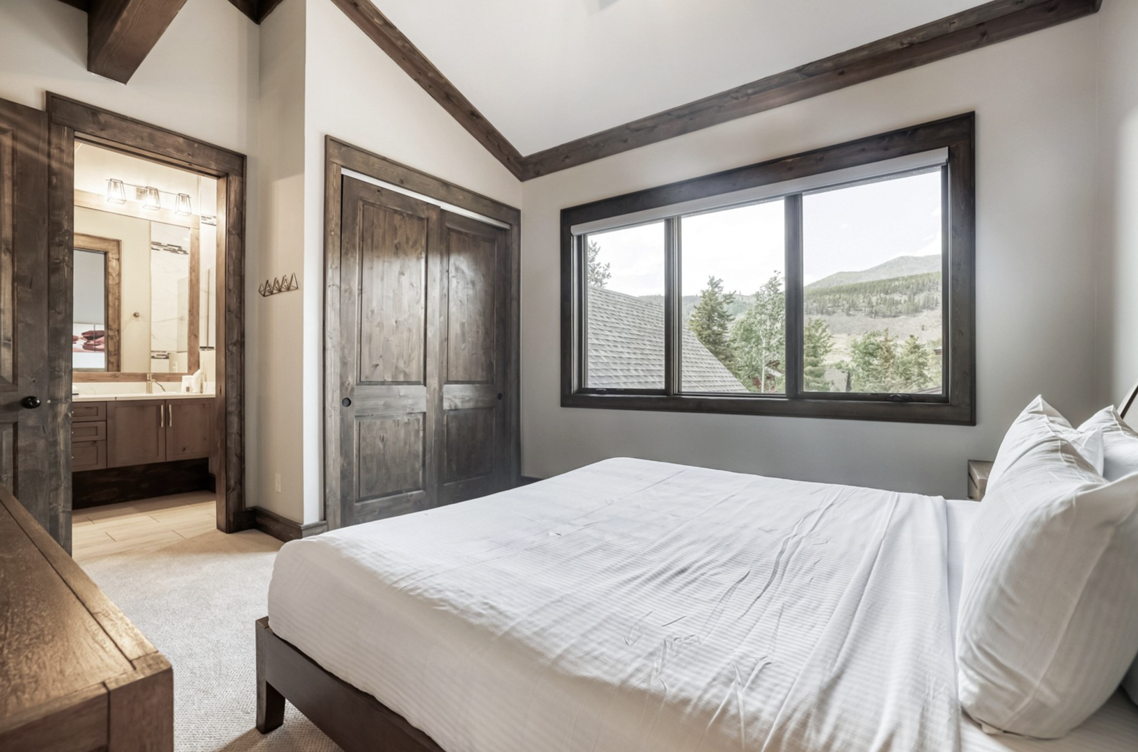 Wake up to stunning mountain vistas framed by your private window. This serene retreat features rustic wood accents, vaulted ceilings with exposed beams, and an ensuite bath—your peaceful escape awaits.