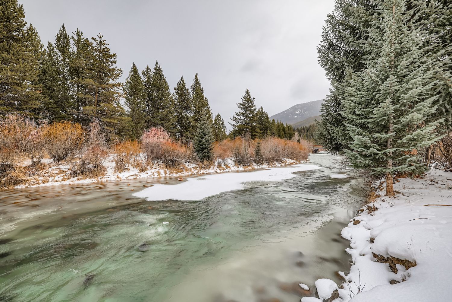 Winter scenery near the property features a flowing river surrounded by snow-covered banks and mountain forest landscape.
