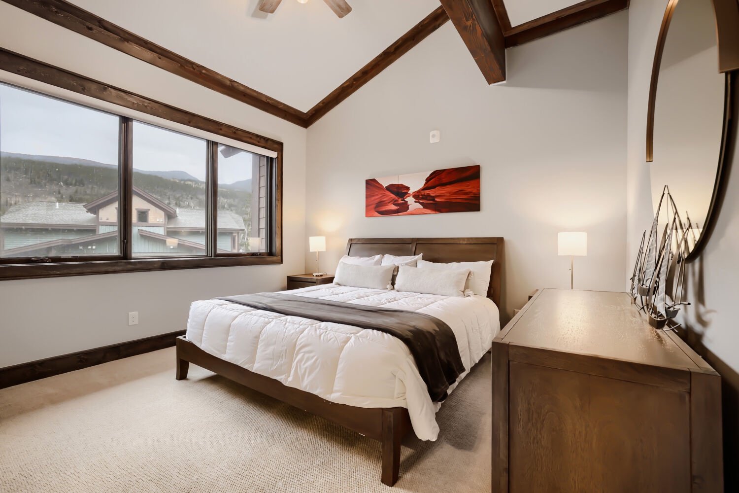 Wake up to stunning mountain views from your bedroom, where crisp linens and warm wood accents create a peaceful mountain retreat beneath soaring timber beams.